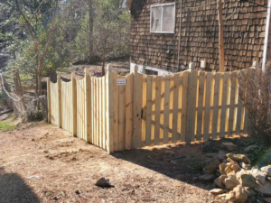 A wooden picket fence with a gate expertly installed on a sloped property by Integrity Construction and Fencing, LLC in Clanton, AL.