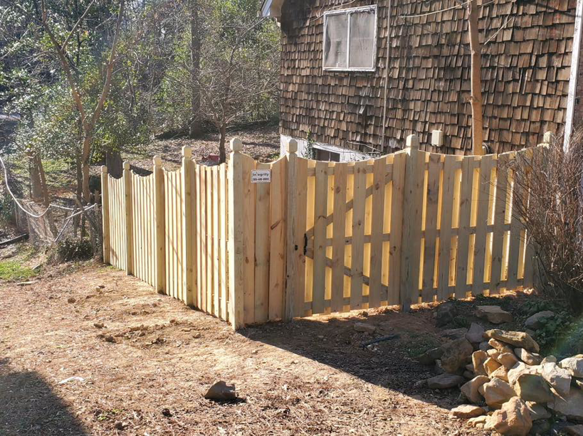 A wooden picket fence with a gate expertly installed on a sloped property by Integrity Construction and Fencing, LLC in Clanton, AL.