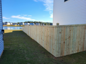 A newly installed wooden picket fence next to a house, offering a view of a pond, by Lundquist Home Improvements in Mount Pleasant, SC.