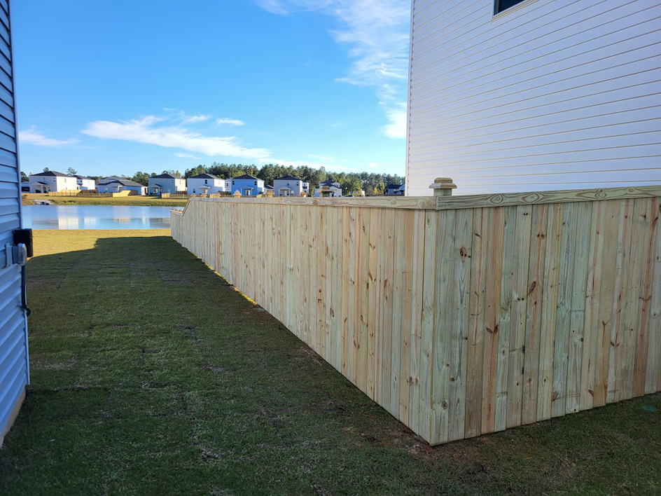 A newly installed wooden picket fence next to a house, offering a view of a pond, by Lundquist Home Improvements in Mount Pleasant, SC.