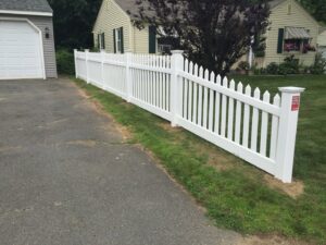 A newly installed wooden picket fence bordering a paved patio next to a residential building by Brodeur-Campbell Fence Co. in Springfield, MA.