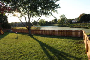 A classic wooden picket fence installed along the edge of a pond by Brothers Fence Co. in Madison, WI.