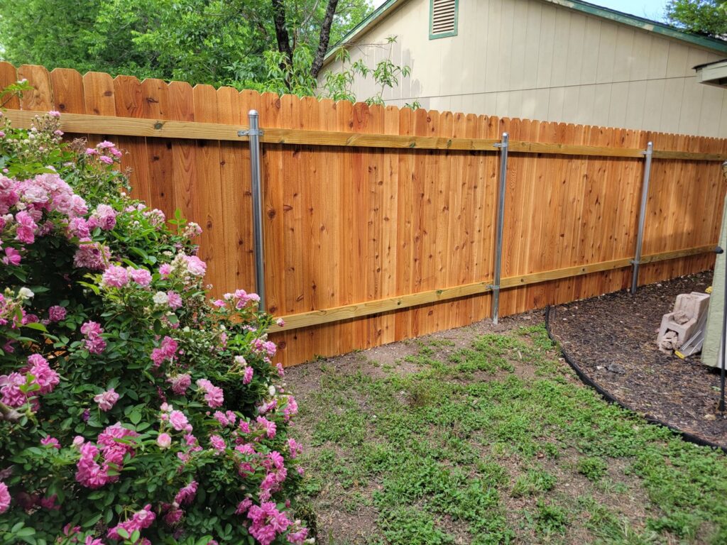 A wooden picket fence with a scalloped top and metal posts next to rose bushes by Landmark Fence & Deck Company in Saint Paul, MN.