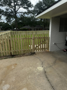A newly installed wooden picket fence with a gate next to a patio area by J&L Fence in Zolfo Springs, FL.