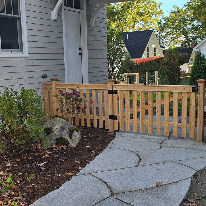 A newly installed wooden picket fence with a gate leading to a home by Midcoast Fence in Northport, ME.