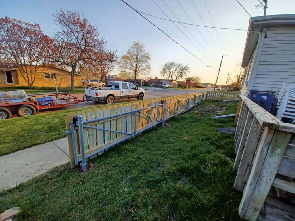 A newly installed wooden picket-style fence with a gate along a roadside by Smith & Company Custom Fence LLC in Niles, MI.