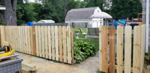 A newly installed wooden picket fence with an open gate in a residential yard by Valkyrie construction, LLC in Granville, OH.