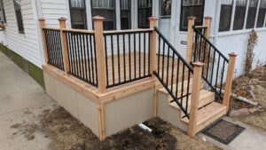 A custom wooden porch with black metal railings and steps installed by Babb Custom Fence in Sioux Falls, SD.