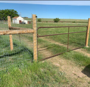 A wooden post and wire fence with a metal gate in a green field, installed by Colorado Springs Fence Company in Colorado Springs, CO.