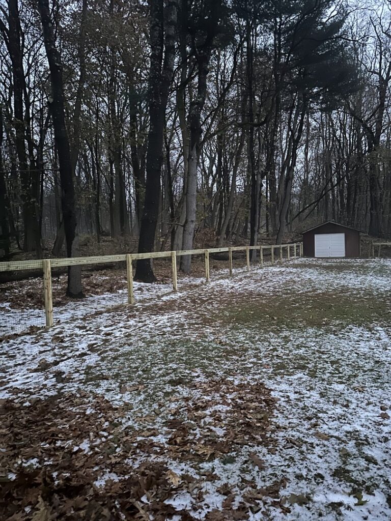 A newly installed wooden post and wire mesh fence in a snowy backyard by Vision One Construction in Schenectady, NY
