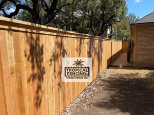 A newly installed wooden privacy fence along a property line with a gate in the distance by Tropical Fencing And Wood Works in Page, TX.