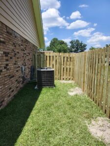 A newly installed wooden privacy fence enclosing an outdoor AC unit next to a brick house by Riggins Renovations LLC in Biloxi, MS.