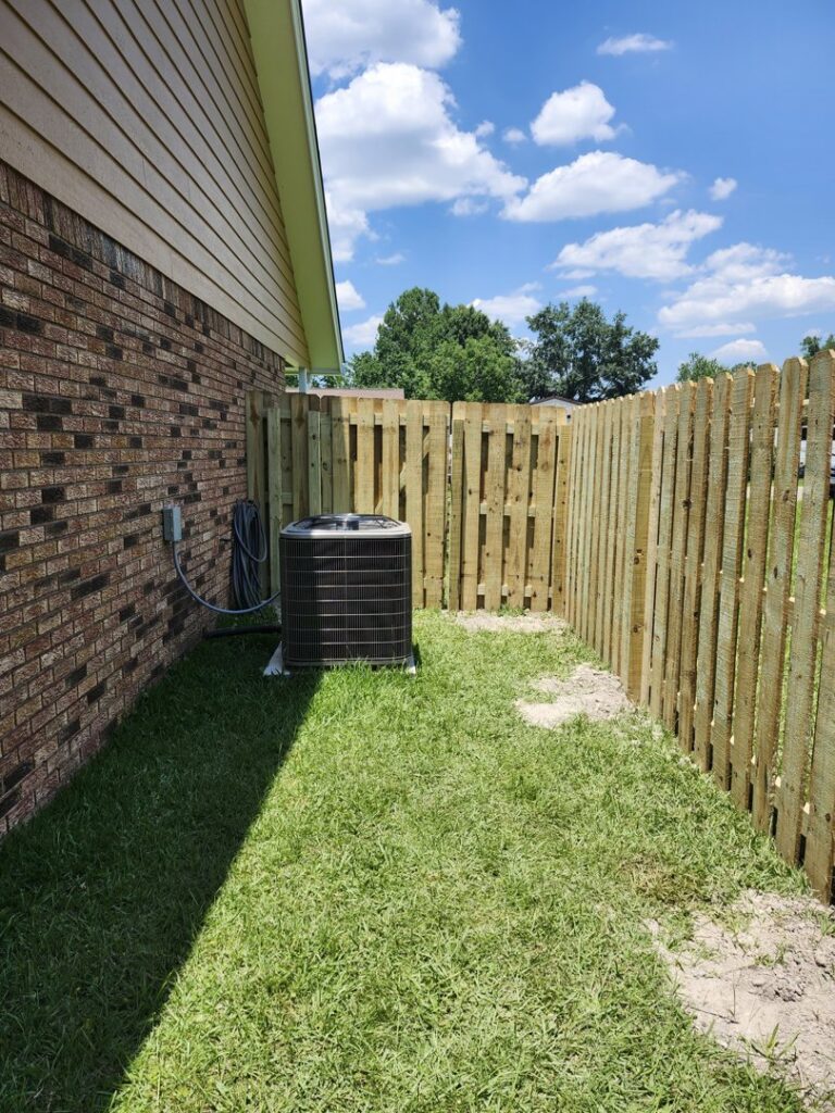 A newly installed wooden privacy fence enclosing an outdoor AC unit next to a brick house by Riggins Renovations LLC in Biloxi, MS.