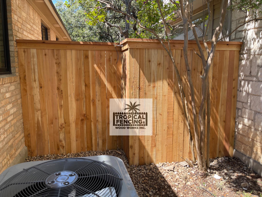A newly installed wooden privacy fence concealing an AC unit next to a house by Tropical Fencing And Wood Works in Page, TX.