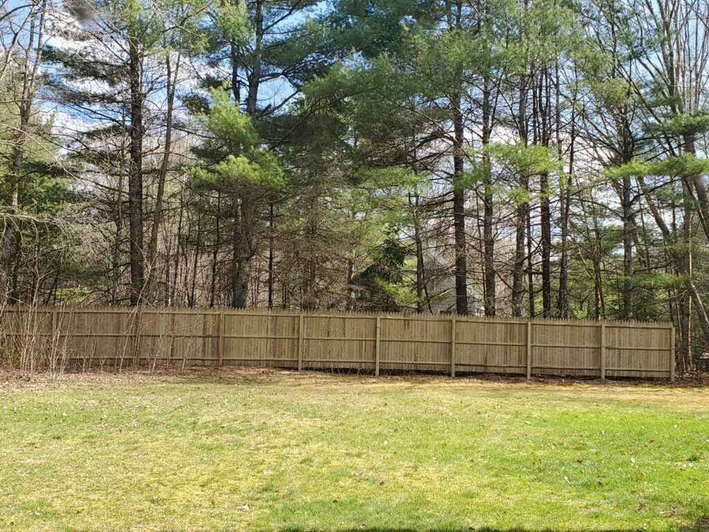 A tall wooden privacy fence installed in a backyard, providing seclusion for a home in Weare, NH by MH Fence.