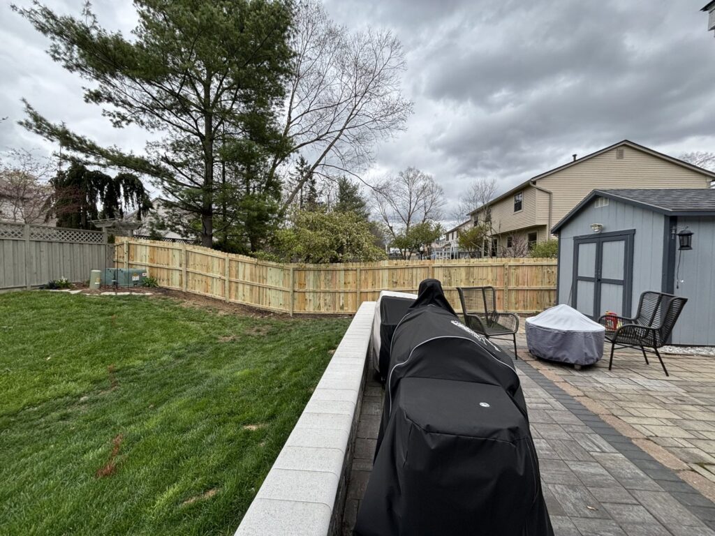 A new wooden privacy fence installed in a backyard with a stone patio, by D&M Renovation Services LLC in Columbus, OH.