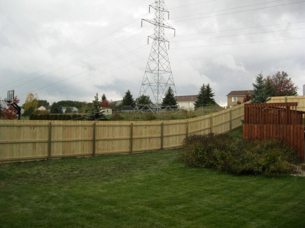 A wooden privacy fence installed in a backyard with power lines visible in the background by Metrofence in Grand Rapids, MI.