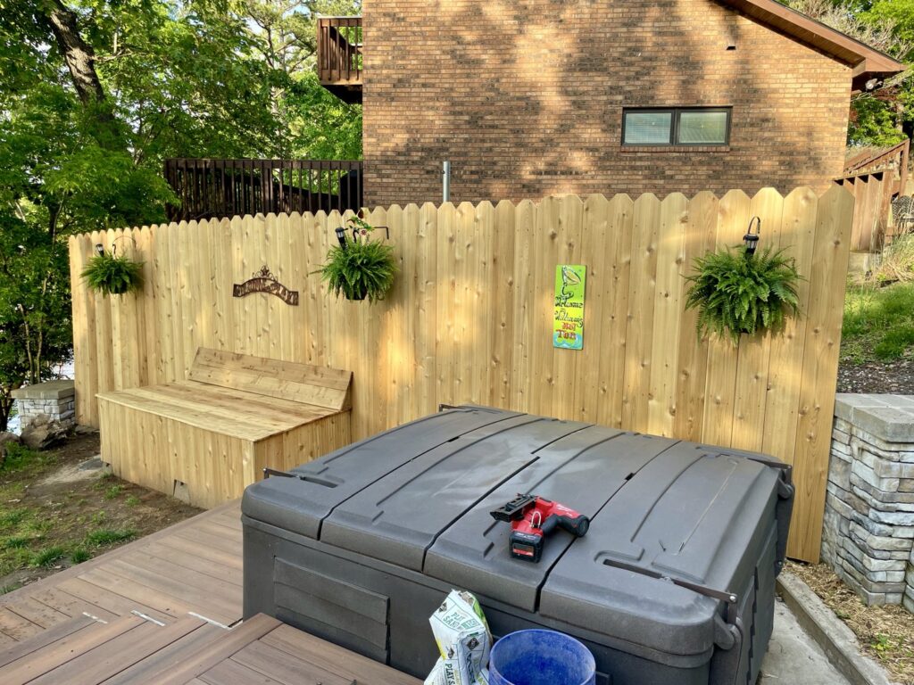 A wooden privacy fence with a decorative top and built-in bench next to a hot tub by Frontline Fence Company in Fulton, NY