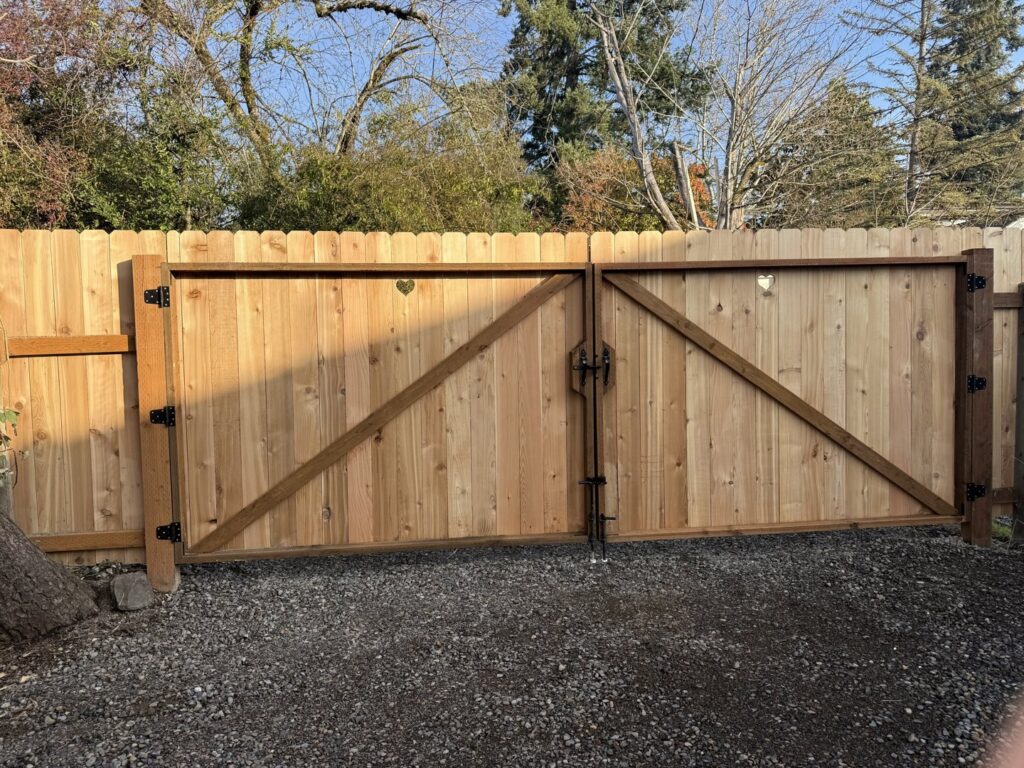 A new wooden privacy fence with a double gate featuring heart cutouts by Pacific Woods Fence and Deck in Springfield, OR.