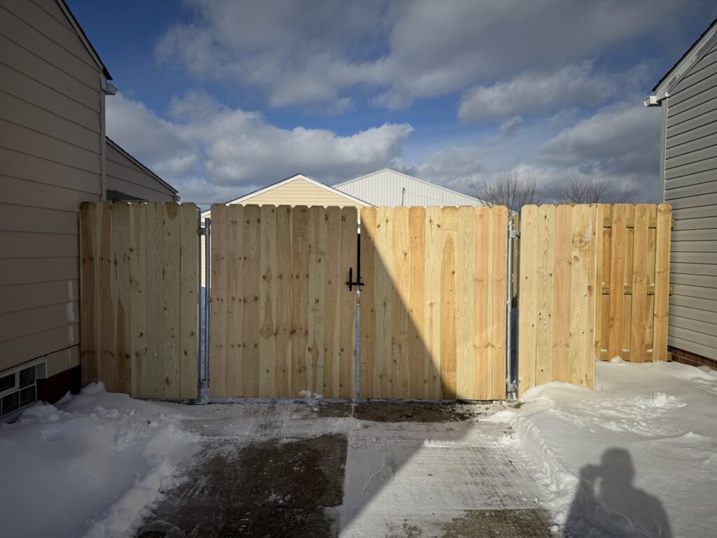 A newly installed wooden privacy fence with a double gate in a snowy backyard by Affordable Fencing in Parma, OH.