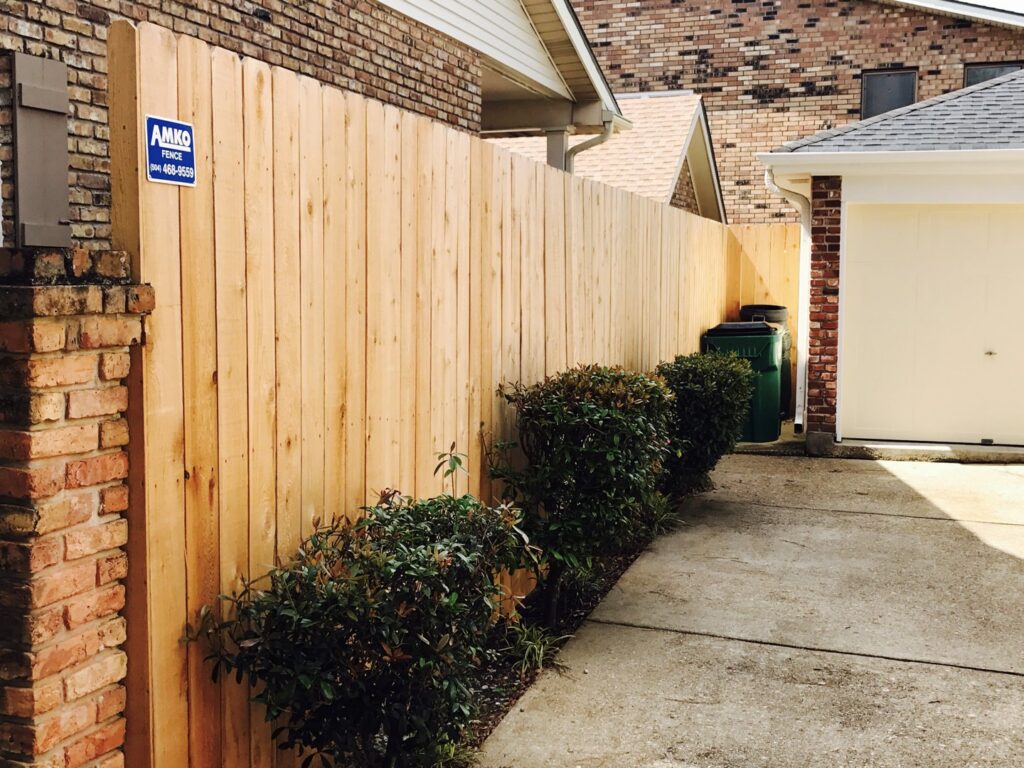 A new wooden privacy fence installed along a driveway next to a brick wall and garage by Amko Fence Co. in Kenner, LA.