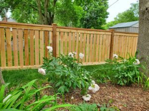 A beautiful wooden privacy fence with a decorative top rail and post caps, complemented by blooming flowers, by Top Notch Fence in East Bethel, MN.