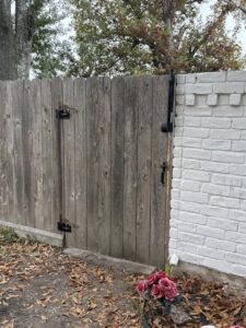 A wooden privacy fence gate next to a white brick wall, installed by Lone Star Pool Fence in Houston, TX.