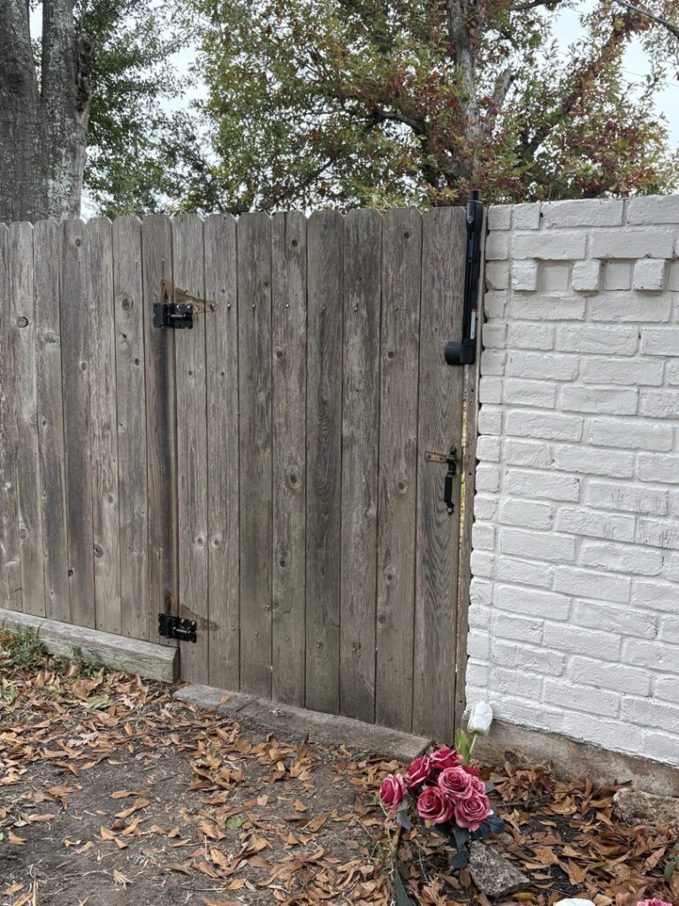 A wooden privacy fence gate next to a white brick wall, installed by Lone Star Pool Fence in Houston, TX.