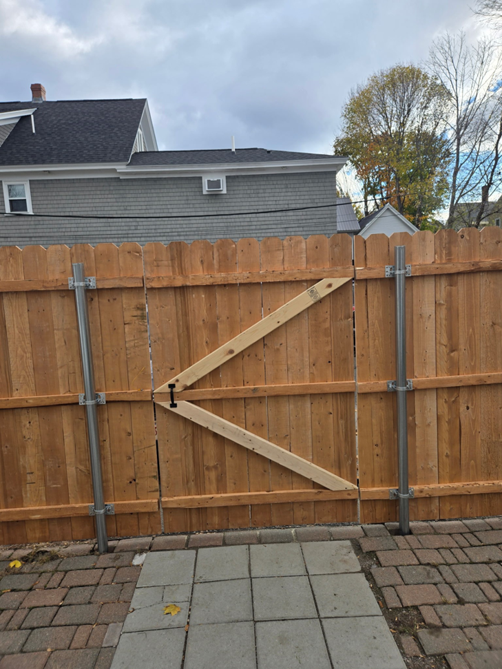 A newly installed wooden privacy fence with a gate and sturdy metal posts by Dore's Fence Company in Greenbush, ME.