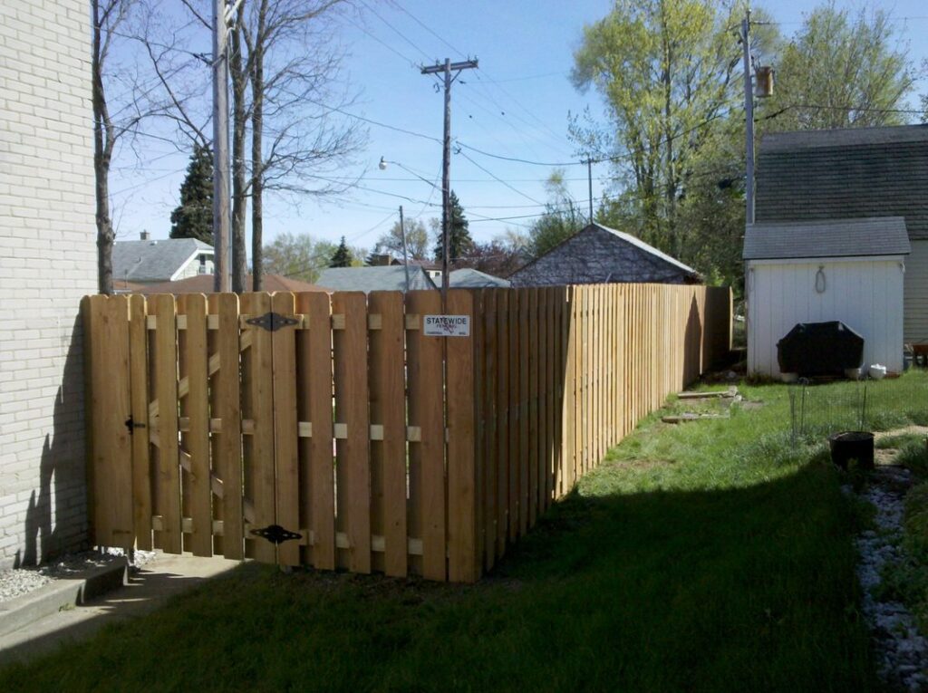 A newly installed wooden privacy fence with a gate in a residential backyard by Statewide Fencing, Inc. in Racine, WI.