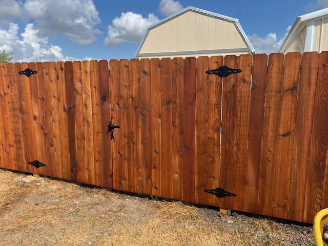 A newly installed wooden privacy fence with a matching gate and decorative hardware by Superior Fence Co. of San Antonio, TX.