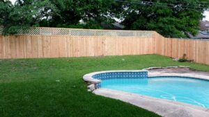 A wooden privacy fence with a decorative lattice top surrounding a swimming pool by Landmark Fence & Deck Company in Saint Paul, MN.