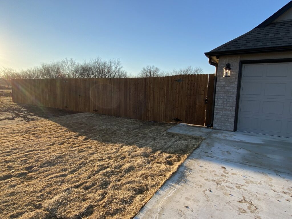 A newly installed wooden privacy fence running alongside a residential house and garage by Ninety-One Services in Tulsa, OK