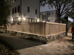 A custom wooden privacy fence installed on top of a stone retaining wall with a gate, completed by AFK FENCE LLC in Waldorf, MD.