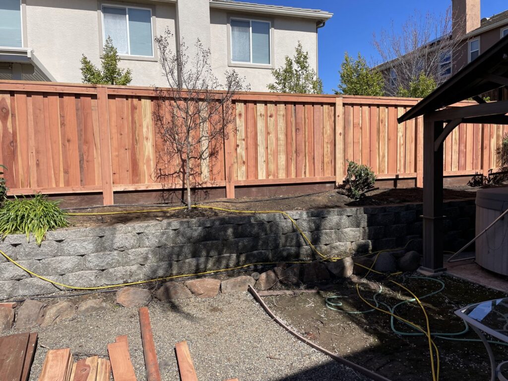 A sturdy wooden privacy fence built atop a stone retaining wall in a backyard, installed by Mega Fence in Thornton, CA.