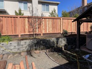 A sturdy wooden privacy fence built atop a stone retaining wall in a backyard, installed by Mega Fence in Thornton, CA.