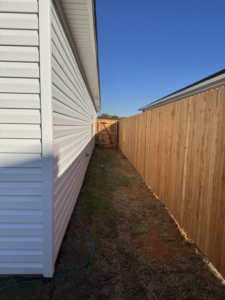 A wooden privacy fence installed along a narrow side yard with a gate at the far end by Frontline Fence Company in Fulton, NY