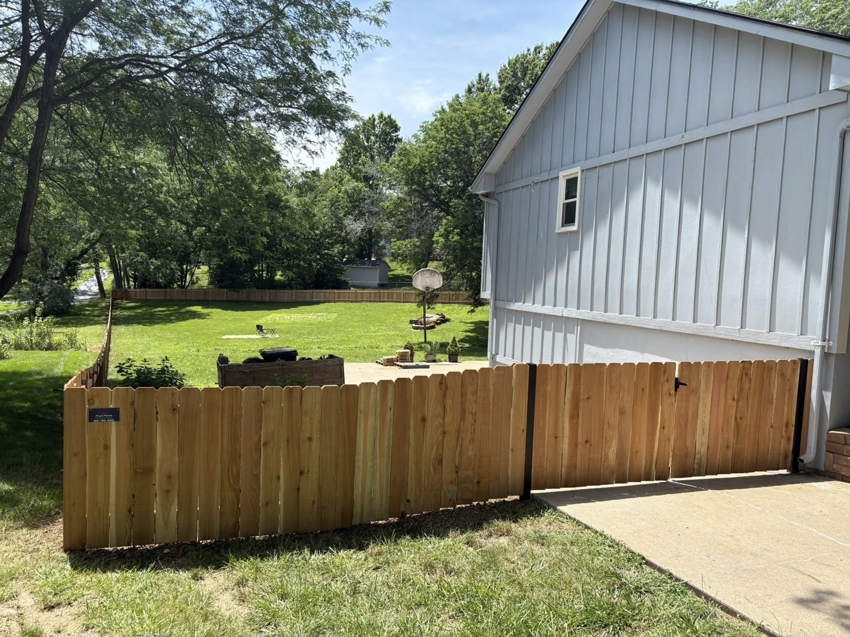 A newly installed wooden privacy fence with a single gate next to a residential house by Fry's Fence LLC in Grain Valley, MO.