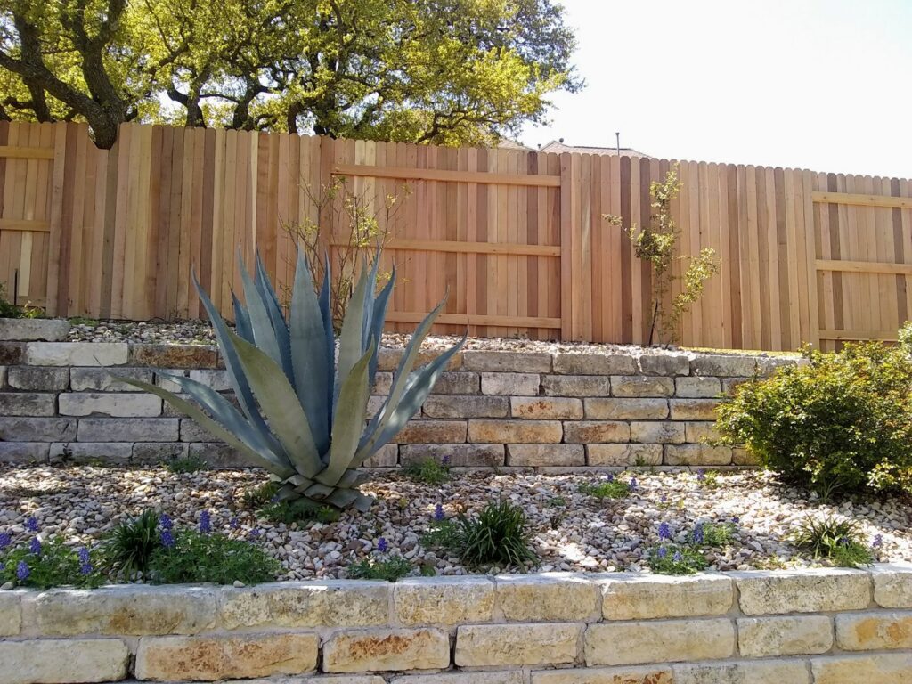 A wooden privacy fence installed behind a stone retaining wall and landscaping by Landmark Fence & Deck Company in Saint Paul, MN.