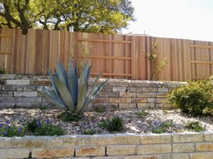 A wooden privacy fence installed behind a stone retaining wall and landscaping by Landmark Fence & Deck Company in Saint Paul, MN.