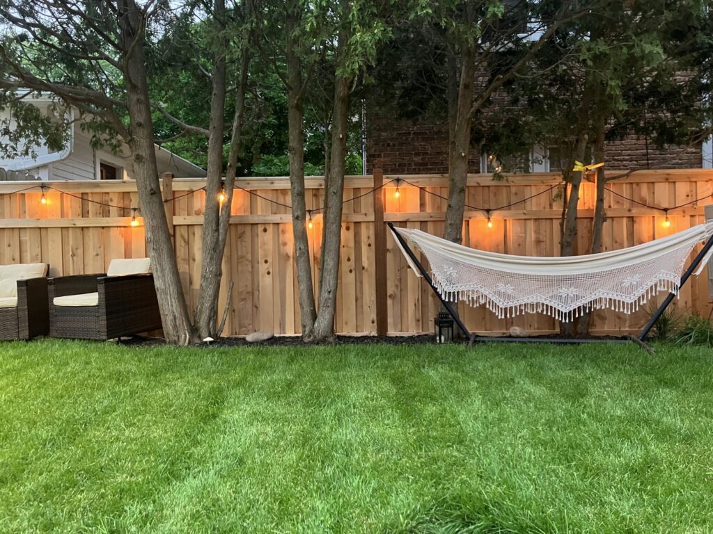 A newly installed wooden privacy fence adorned with string lights in a backyard by Chisel + Vine in Milwaukee, WI.