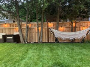 A newly installed wooden privacy fence adorned with string lights in a backyard by Chisel + Vine in Milwaukee, WI.