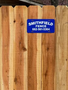 A newly installed wooden privacy fence with a Smithfield Fence business sign in Crowder, MS.