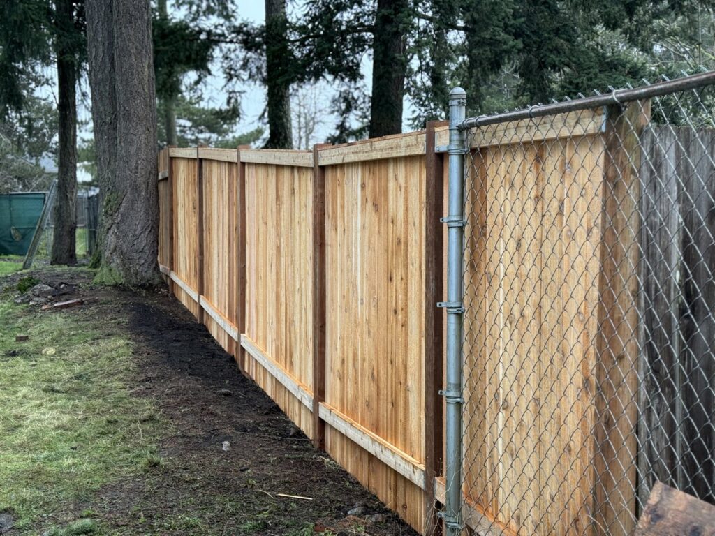 A new wooden privacy fence installed alongside an existing chain-link fence by Fences NW LLC in Spanaway, WA