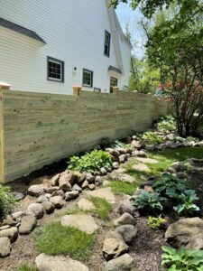A wooden privacy fence with decorative post caps, bordering a landscaped garden, installed by NBBJ Fence LLC in Bluffton, IN.