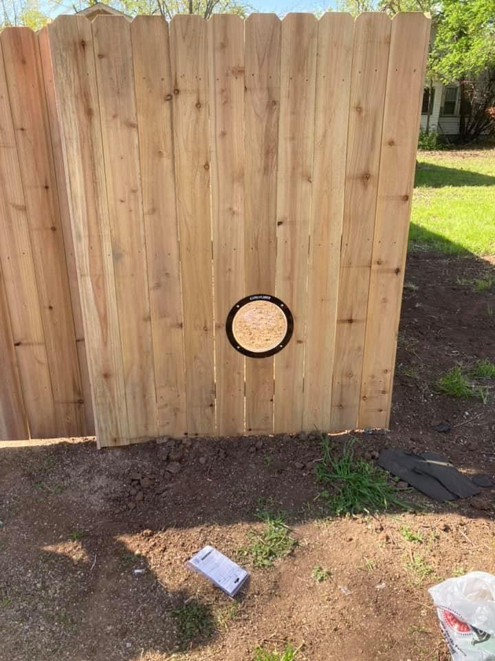 A custom wooden privacy fence featuring a unique dog window, installed by Pokey Fencing & Masonry in Stillwater, OK.