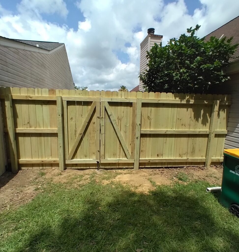 A newly installed wooden privacy fence with a sturdy double gate in a residential backyard by Riggins Renovations LLC in Biloxi, MS.
