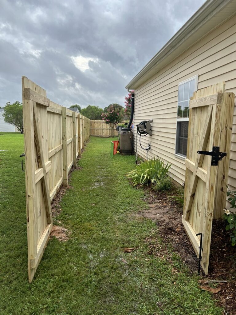 A wooden privacy fence featuring double gates installed alongside a house by Align Fence Builders in Durham, NC.