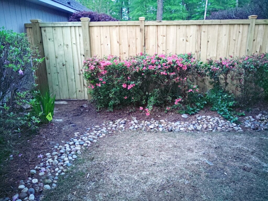 A wooden privacy fence with a gate, surrounded by lush landscaping, installed by Kelley Fence and Gate in Eva, AL.