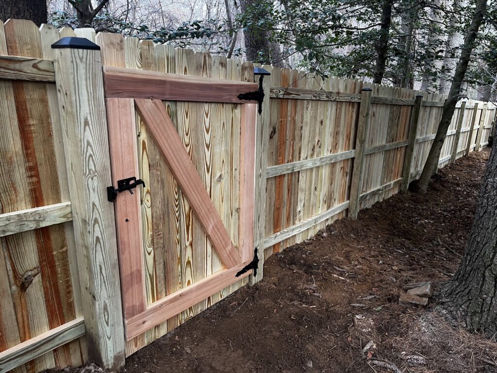 A newly installed wooden privacy fence with a custom gate in a wooded residential area by AFK FENCE LLC in Waldorf, MD.